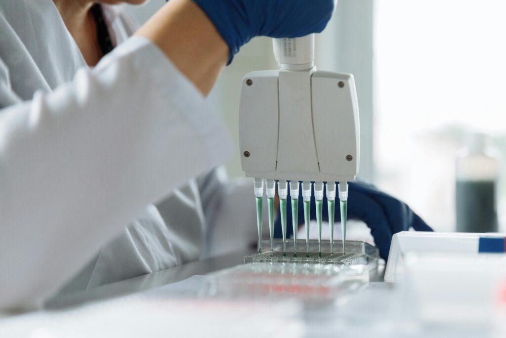 A scientist wearing a lab coat uses a multichannel pipette for liquid handling in a lab setting.
